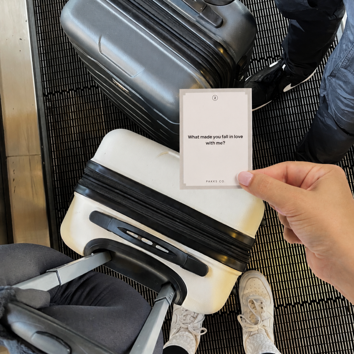 A hand holding up a Go Deeper card reading "What made you fall in love with me?" above two suitcases