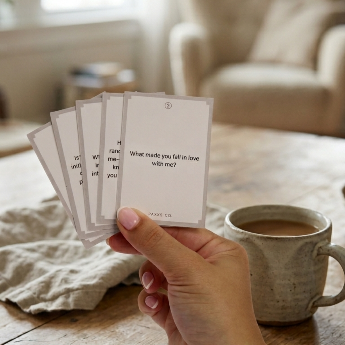A hand fanning Go Deeper cards reading "What made you fall in love with me?" beside a mug of coffee