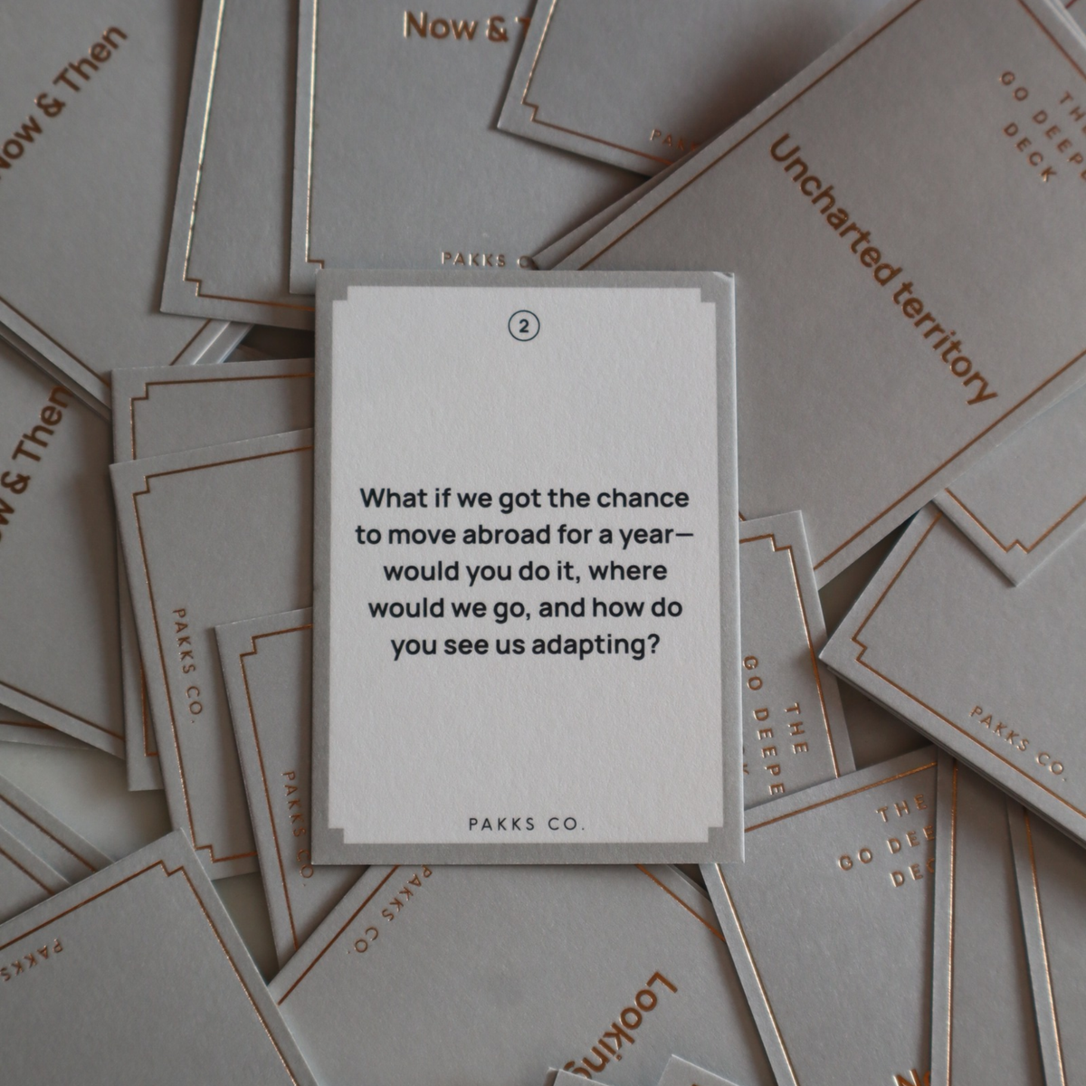 A Go Deeper card asking about moving abroad for a year, on a pile of "Now & Then" and "Uncharted territory" cards