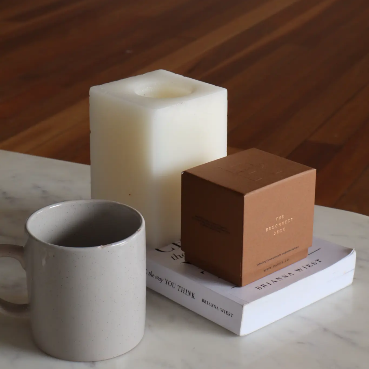 The terracotta Reconnect Deck box on a book beside a candle and a mug on a marble table