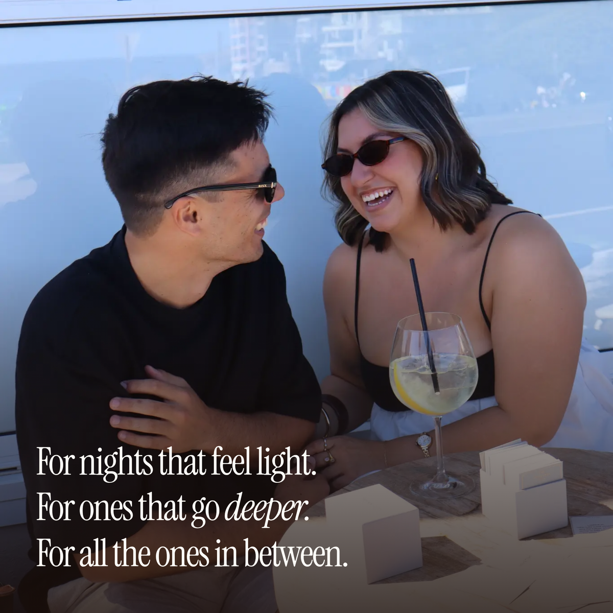 A couple laughing at an outdoor table, captioned "For nights that feel light. For ones that go deeper."